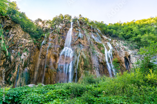 Waterfall and blue crystalline water in Plitvice Nation Park  Croatia  in a sunny day in summer during vacations immersed in wild nature with rocks trees flowers and forests
