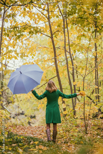 Woman holding umbrella and fall leafs while standing in the park. 