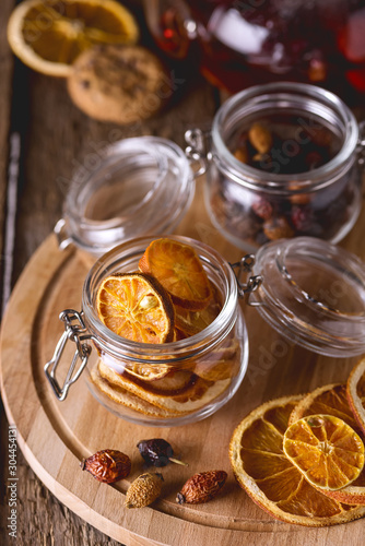Glass Jars of Dried Citrus and Berry for Tea Ingredients for Tasty Hot Beverage Wooden Tray Wooden Background Dried Oranges Vertical Above Toned