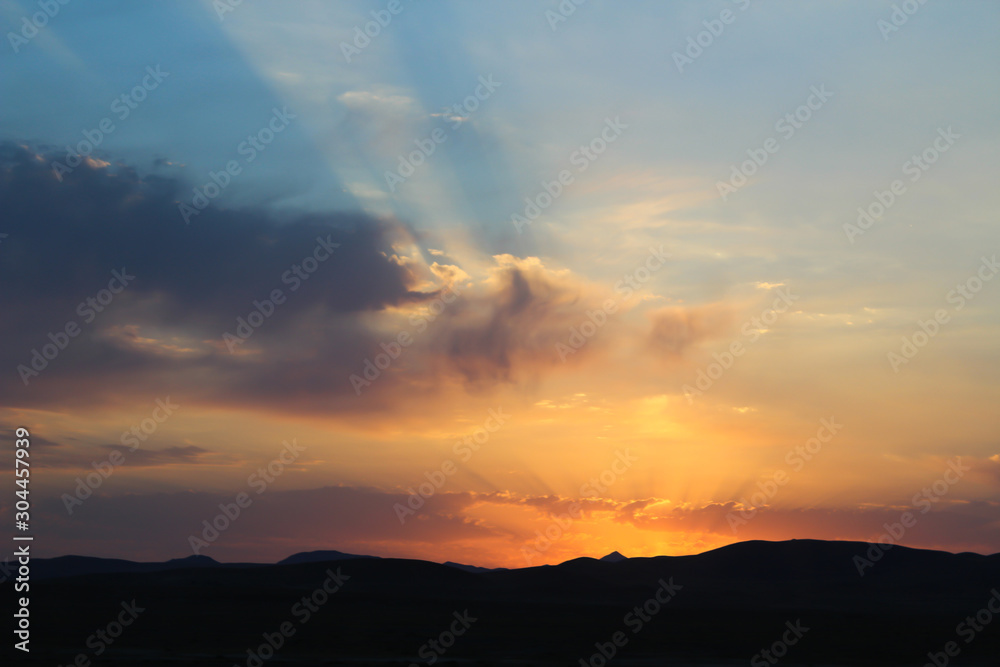 Sunrise shines reflected on golden clouds behind the mountains.