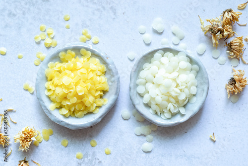 yellow and white cosmetic beeswax pellets in white ceramic bowl for homemade natural beauty and D.I.Y. project. photo