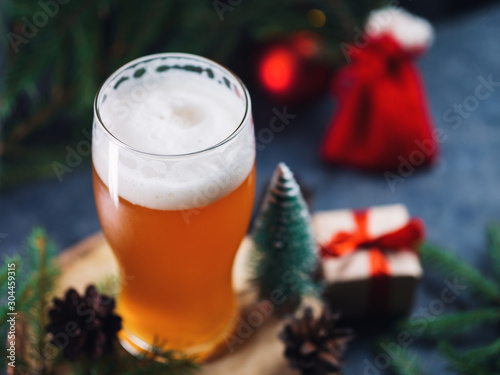 фотография A glass of Christmas beer on the table with gifts and branches of the tree