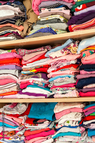 A wardrobe full of childrens clothes creative background texture. Lots of rows of colorful kids clothing laying neatly aligned in the drawer, house closet storage filled with baby shirts, frontal view © Tomasz