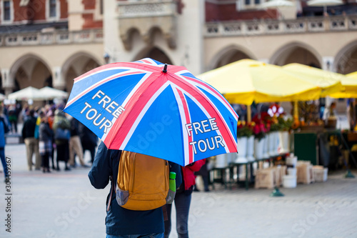 Free tour on a Cracow market square, a UK english guide with a united kingdom flag umbrella seen from the back. Local free of charge tourist guides. Tourism, travelling for england residents concept © Tomasz