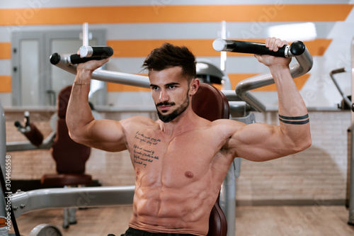 Shirtless muscular young man doing barbell bench press exercise at the gym