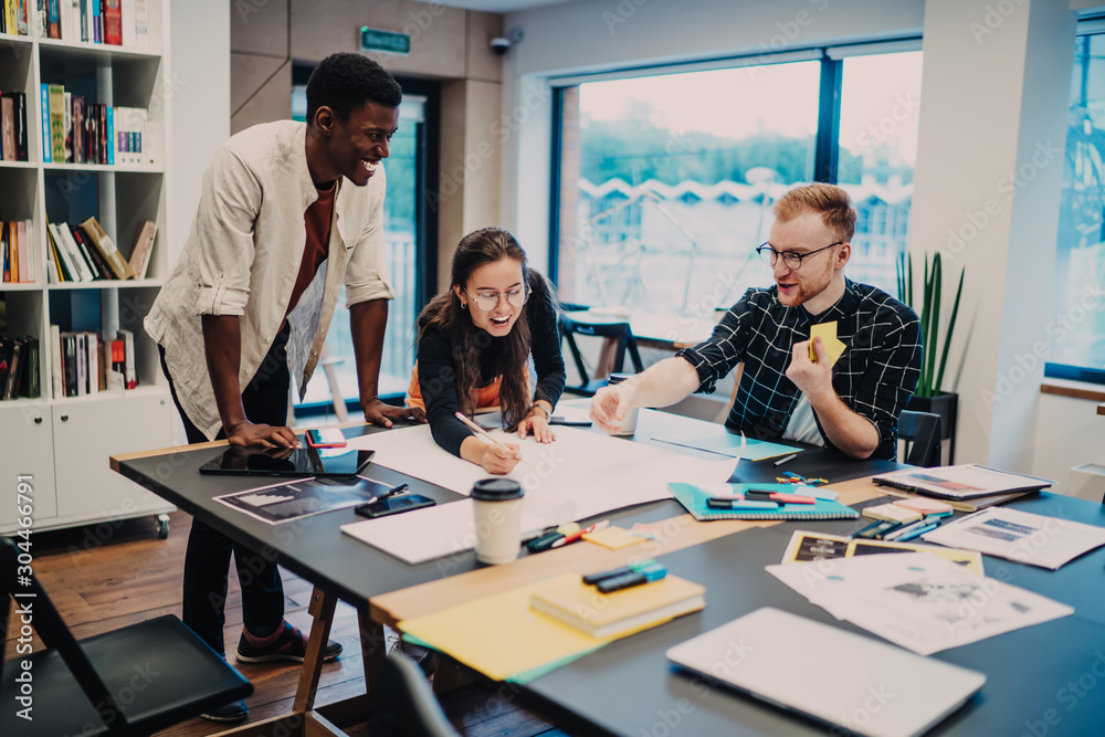 Fototapeta premium Young cheerful colleagues drawing plan