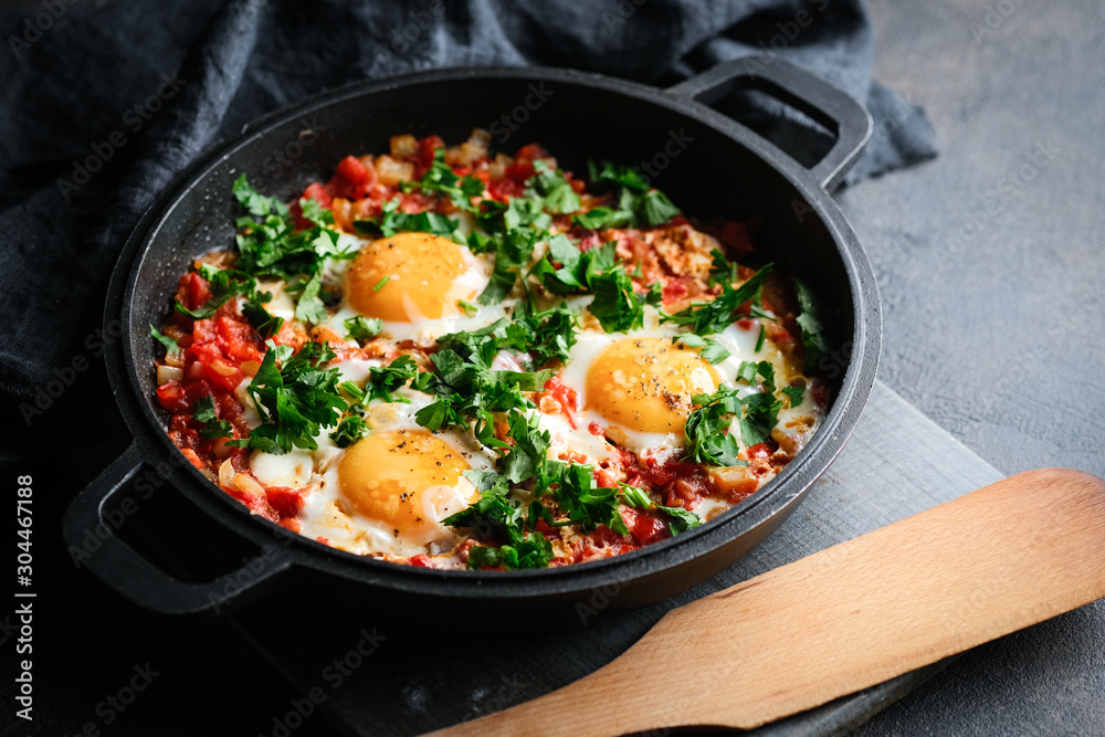 Traditional shakshuka with eggs, tomato, and parsley in a iron pan on a dark background Traditional shakshuka with eggs, tomato, and parsley in a iron pan on a dark background