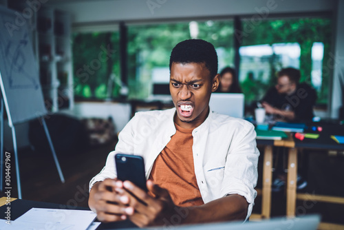 Shocked black man watching phone in office