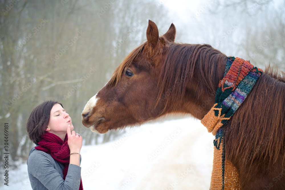 girl kissing red trakehner stallion horse with scarf in the winter