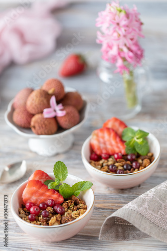 Spring Breakfast with granola and fresh strawberries and lychee and flowers on wooden background.