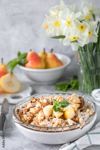 Baked pear crumble with pears and honey in a white dish on the table with copper utensils and flowers