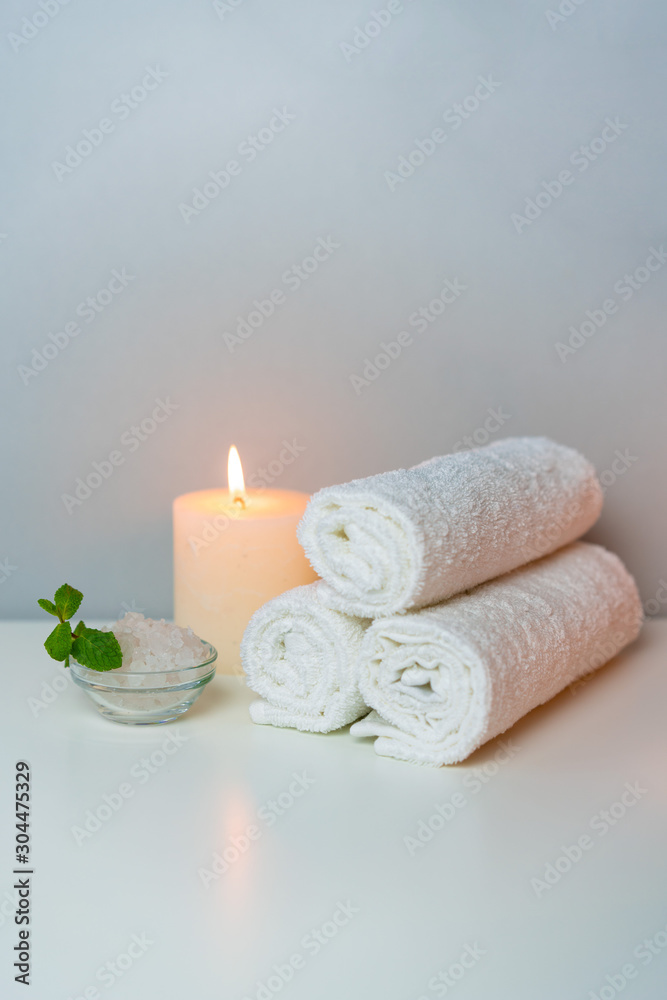 Wellness and SPA concept photo with white towels stack, candle light, sea salt and mint leaf, vertical orientation. Wellness and SPA concept photo with white towels stack, candle light, sea salt and mint leaf, vertical orientation.