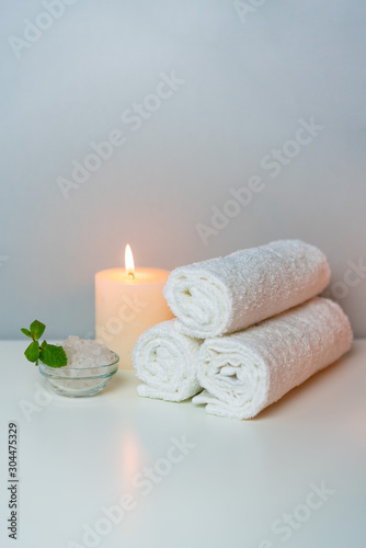Wellness and SPA concept photo with white towels stack, candle light, sea salt and mint leaf, vertical orientation.