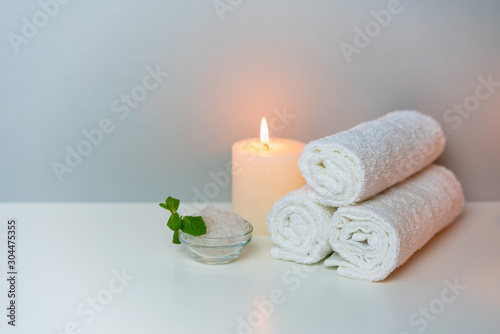 SPA and wellness concept photo with white towels stack, candle light, sea salt and mint leaf, horizontal orientation.