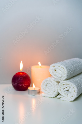 Massage&SPA concept photo with candle lights and stack of white towels, vertical orientation.
