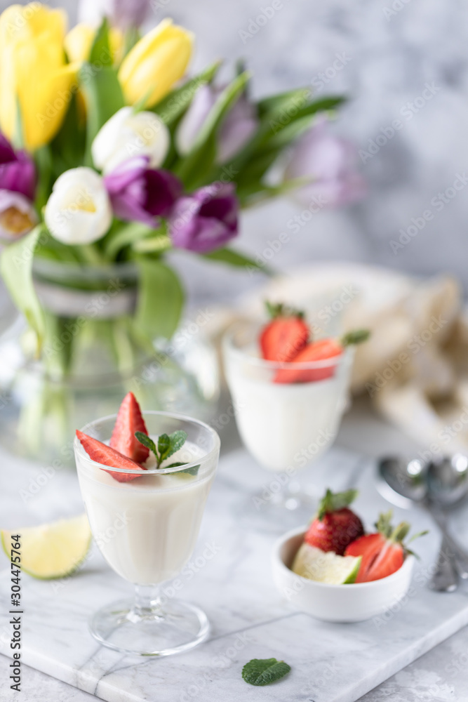 Panna cotta in glass glasses with strawberries on a light background. Bouquet of tulips on a white table. Panna cotta in glass glasses with strawberries on a light background. Bouquet of tulips on a white table.