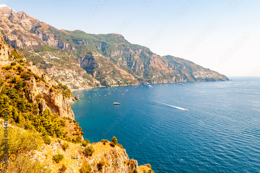 Obraz premium Beautiful scenic landscape of Positano. Rocky coastline full of boats and yachts traveling near high mountains. Cityscape of Positano surrounded by hills and deep blue Tyrrhenian sea waters