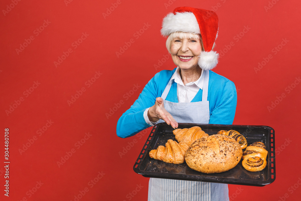 Portrait of pretty charming cheerful aged woman with wrinkle showing gesturing sweet homemade bakery products isolated on red background, christmas recipes. Portrait of pretty charming cheerful aged woman with wrinkle showing gesturing sweet homemade bakery products isolated on red background, christmas recipes.
