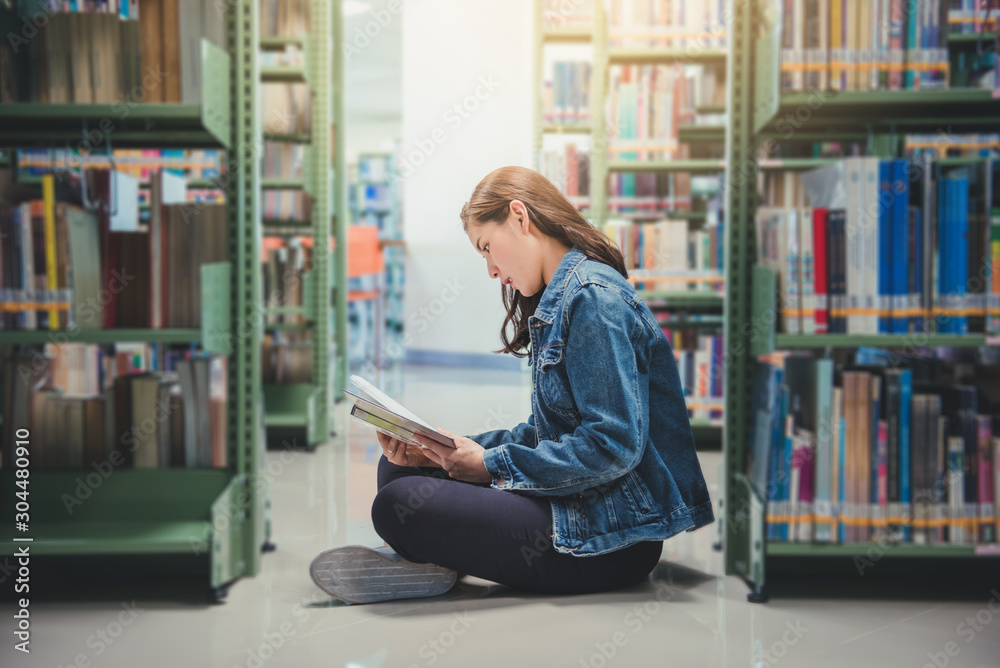 Asian young woman student reading a book nearly bookshelf in library. education concept. Asian young woman student reading a book nearly bookshelf in library. education concept.