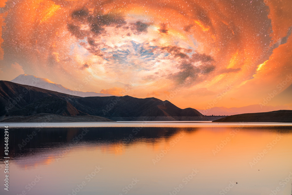 Beautiful scenery after sunset. Colorful spiral clouds in the sky above the lake and mountains.