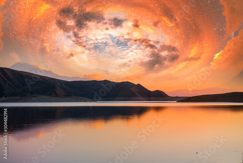 Beautiful scenery after sunset. Colorful spiral clouds in the sky above the lake and mountains.