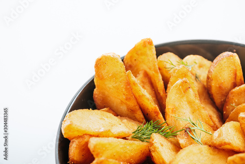 close up view of delicious golden potato wedges with dill in bowl isolated on white