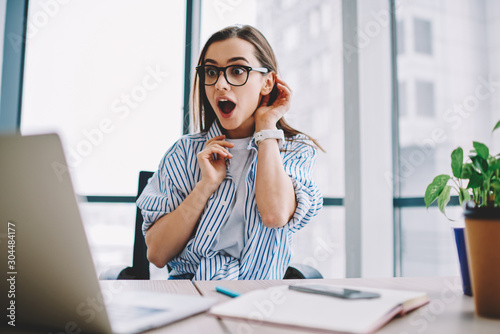 Emotional hipster girl surprised with getting victory in online contest reading news from laptop computer ,expressive young woman open mouth checking discounts for online shopping sitting at desktop . photo