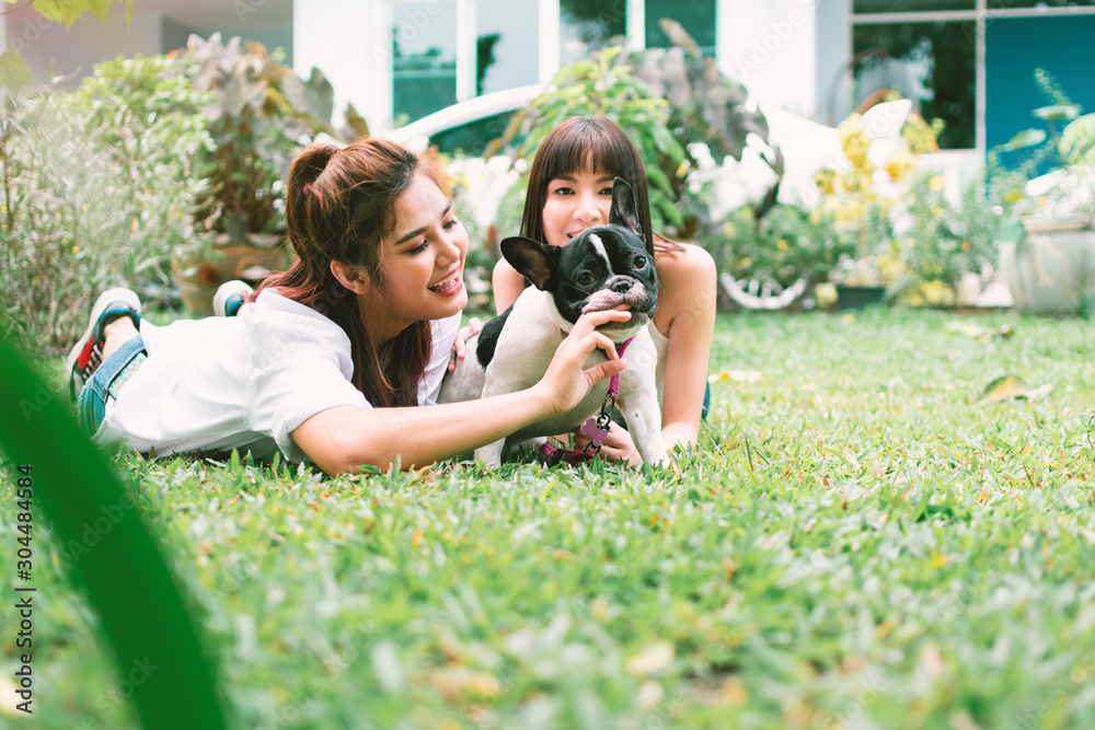 Fototapeta premium Portrait of happy family in back yard at home, Two young beautiful women with french bulldog lay down on lawn to play with her dog.
