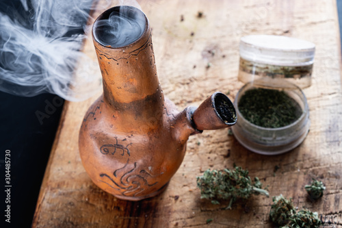Foto Old bong and open cannabis grinder with chopped weed and marijuana in smoke