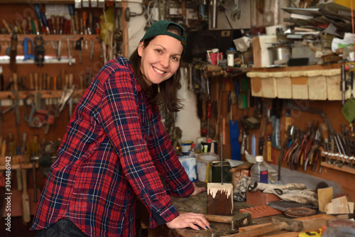 Smiling woman posing in the small workshop with a lot off different tools