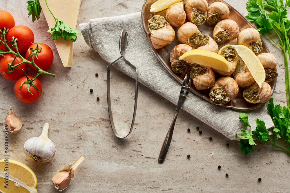 Fototapeta premium top view of delicious served escargots near fresh ingredients on stone background