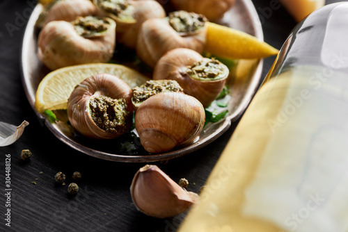 close up view of delicious cooked escargots with lemon slices near white wine