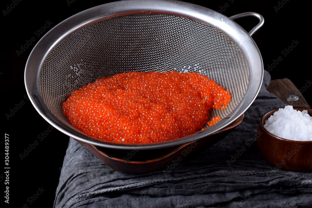 Freshly salted red caviar in a sieve against the black background. Seafood salted at home