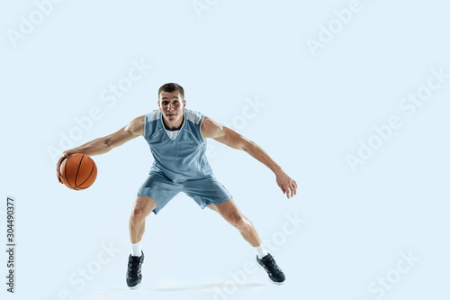 Passioned for. Young caucasian basketball player of team in action, motion in jump isolated on blue background. Concept of sport, movement, energy and dynamic, healthy lifestyle. Training, practicing.