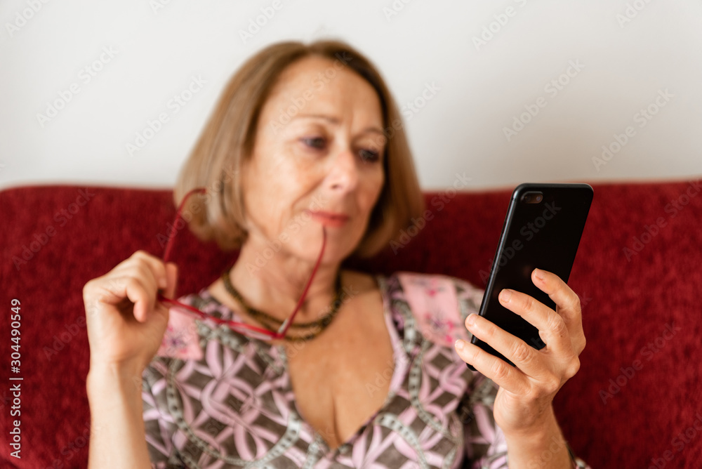 Elegant mature woman using smartphone while sitting on the sofa Elegant mature woman using smartphone while sitting on the sofa