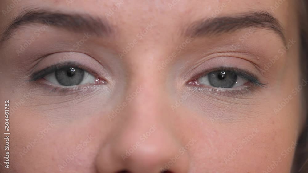 Close up of  attractive woman with gray eyes looking at the camera. Light skin female blinks while staring in the front  Studio light reflects on lady's cornea