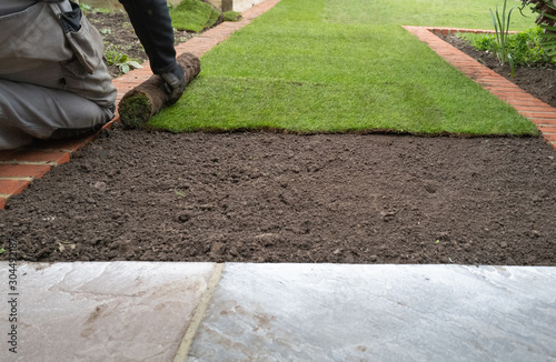 New grass turf being installed in a garden along new brick edging.