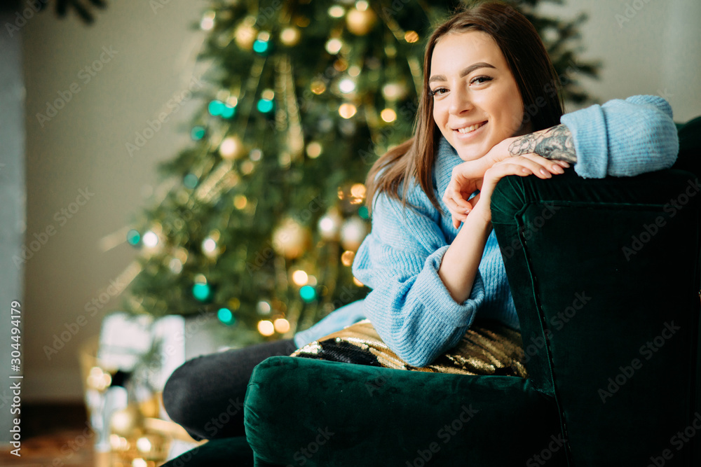 Happy woman with tattoo sits against background of Christmas tree. Happy woman with tattoo sits against background of Christmas tree.