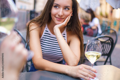 Romantic couple drinking white wine at outdoors table restaurant. Focus on the eyes of the young girl wathing her boyfriend in his eyes. Little smile in the face. photo