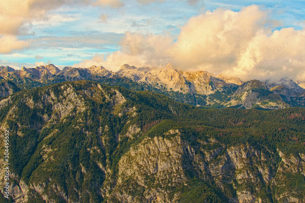 Astonishing landscape of mountain range during sunset. Some mountain peaks are covered with thick white clouds which backlit by the sun. Concept of landscape and nature. Triglav National Park,Slovenia