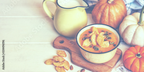 Pumpkin creamy soup served in individual pots, top view. Spoon and bread slice. Delicious colourful orange pumpkin soup for the cold fall weather with scattered pumpkin seeds. Rustic dinner table.