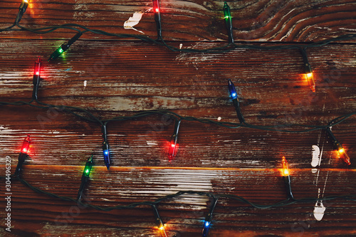 Christmas background concept. New year decoration lights, garland with many small lamps of different color shine on brown grunged wooden table. Top view, flat lay, copy space.