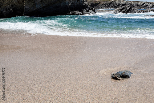 Pedra isolada na areia da praia na zona de rebentação das ondas.