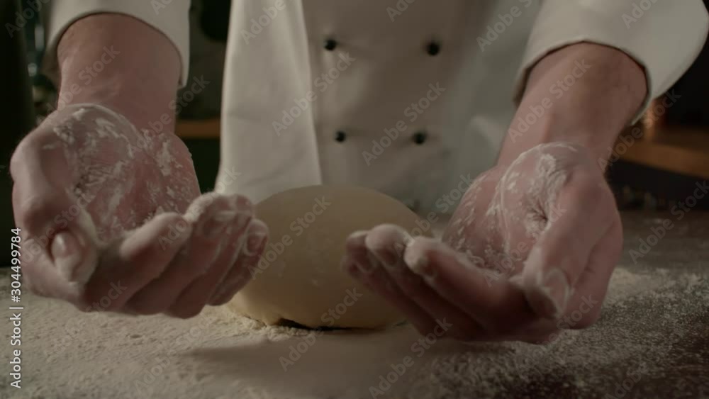 Cook kneads dough with flour on kitchen table, cooking in slow motion side view Cook kneads dough with flour on kitchen table, cooking in slow motion side view