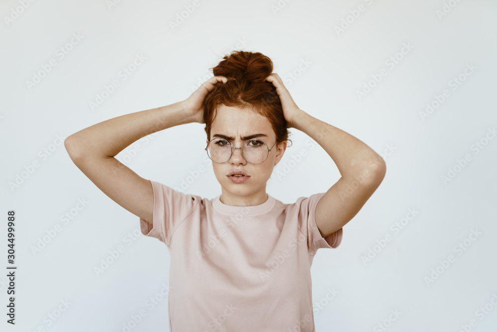 A scoffing schoolgirl strictly looks through her glasses for sight. gray background