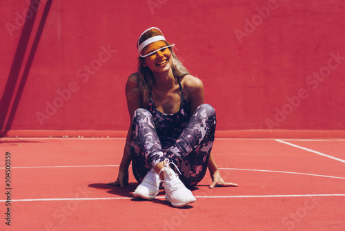 girl in a visor and sportswear sitting cross-legged on the court