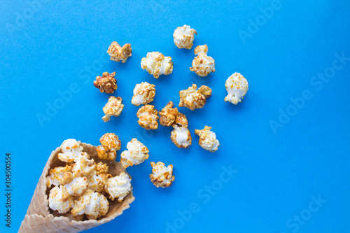 Fototapeta Naklejka Na Ścianę i Meble -  Ice cream cone with caramel popcorn on  the blue  background. Top view. Copy space.