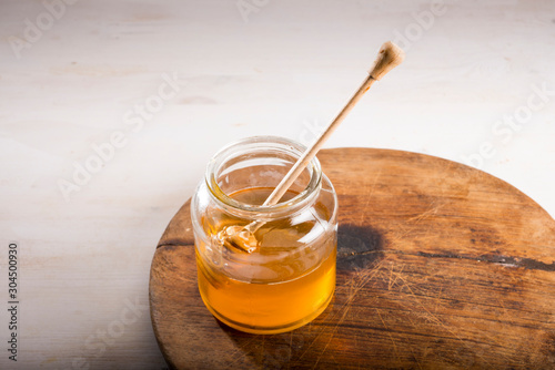 Honey and dipper in glass jar on a wooden floor