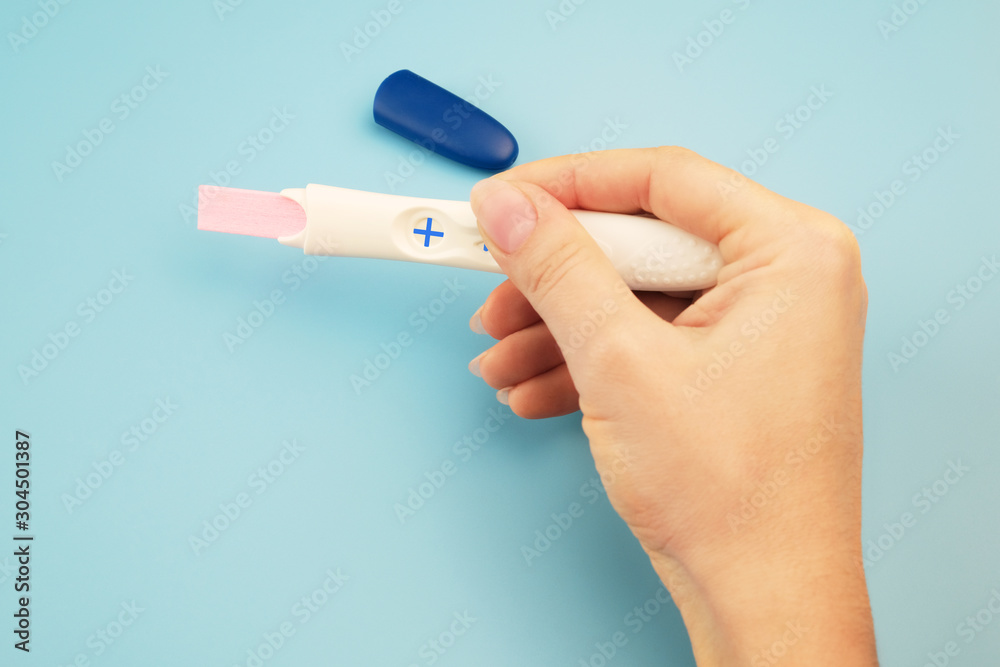 Closeup of a woman's hand with a positive pregnancy test on a blue background. Closeup of a woman's hand with a positive pregnancy test on a blue background.