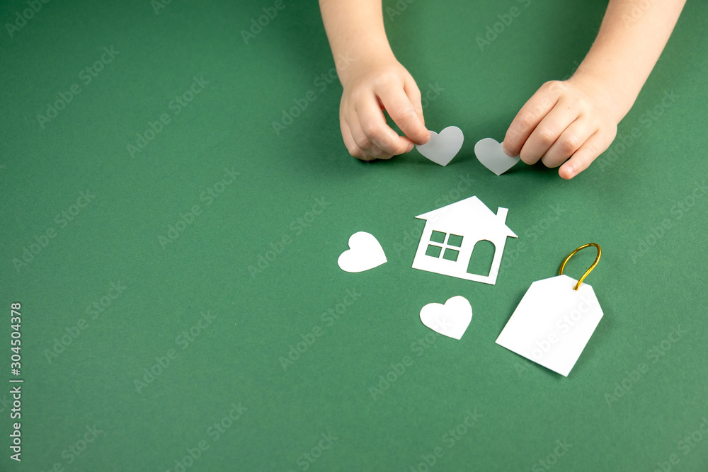 Child hands holding white paper house and heart on green background. Family home and real estate concept. Flat lay, copy space Child hands holding white paper house and heart on green background. Family home and real estate concept. Flat lay, copy space